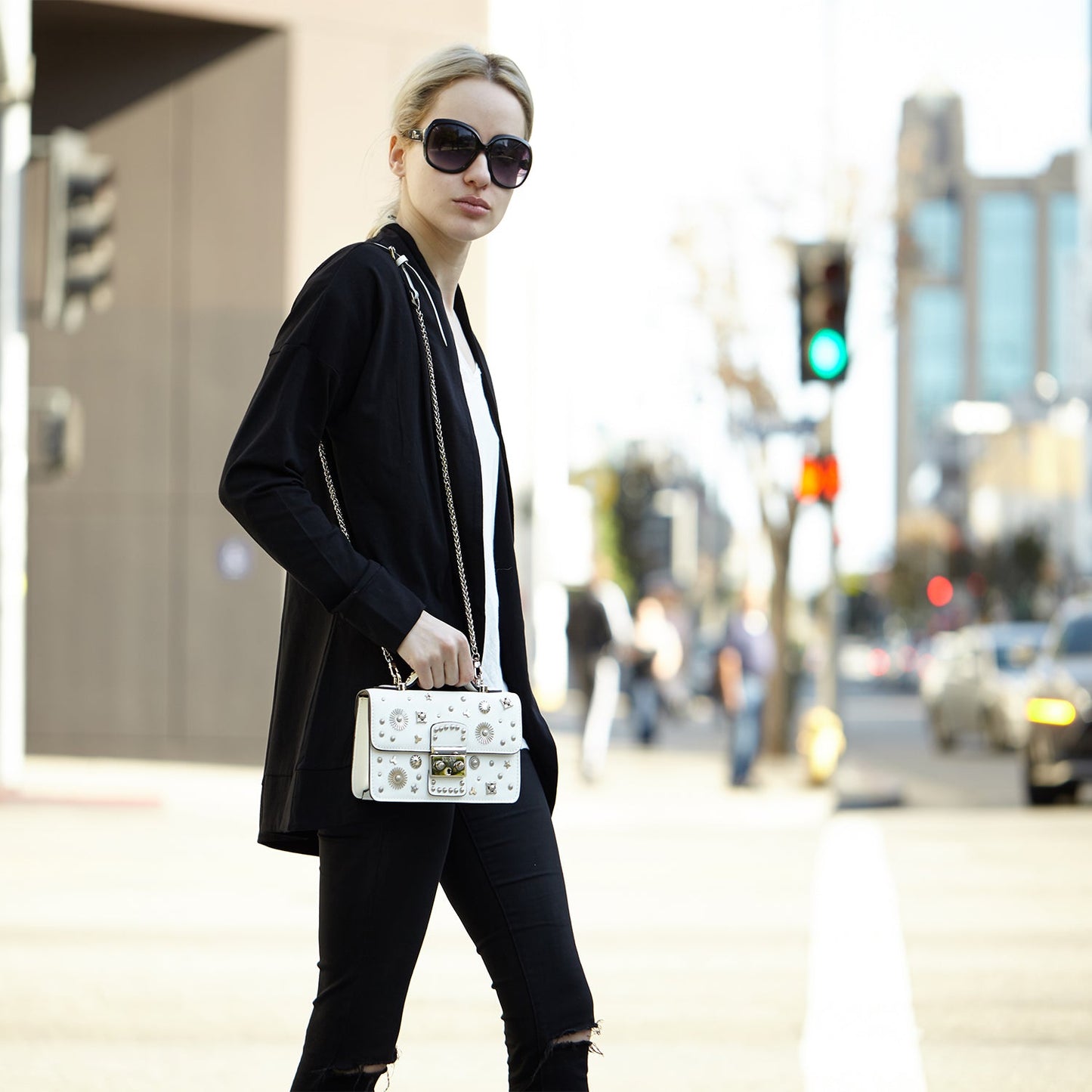 The Hollywood White Leather Crossbody Bag by SUSU features silver stud embellishments, a chain strap, a top handle, and a front clasp with the SUSU brand name.