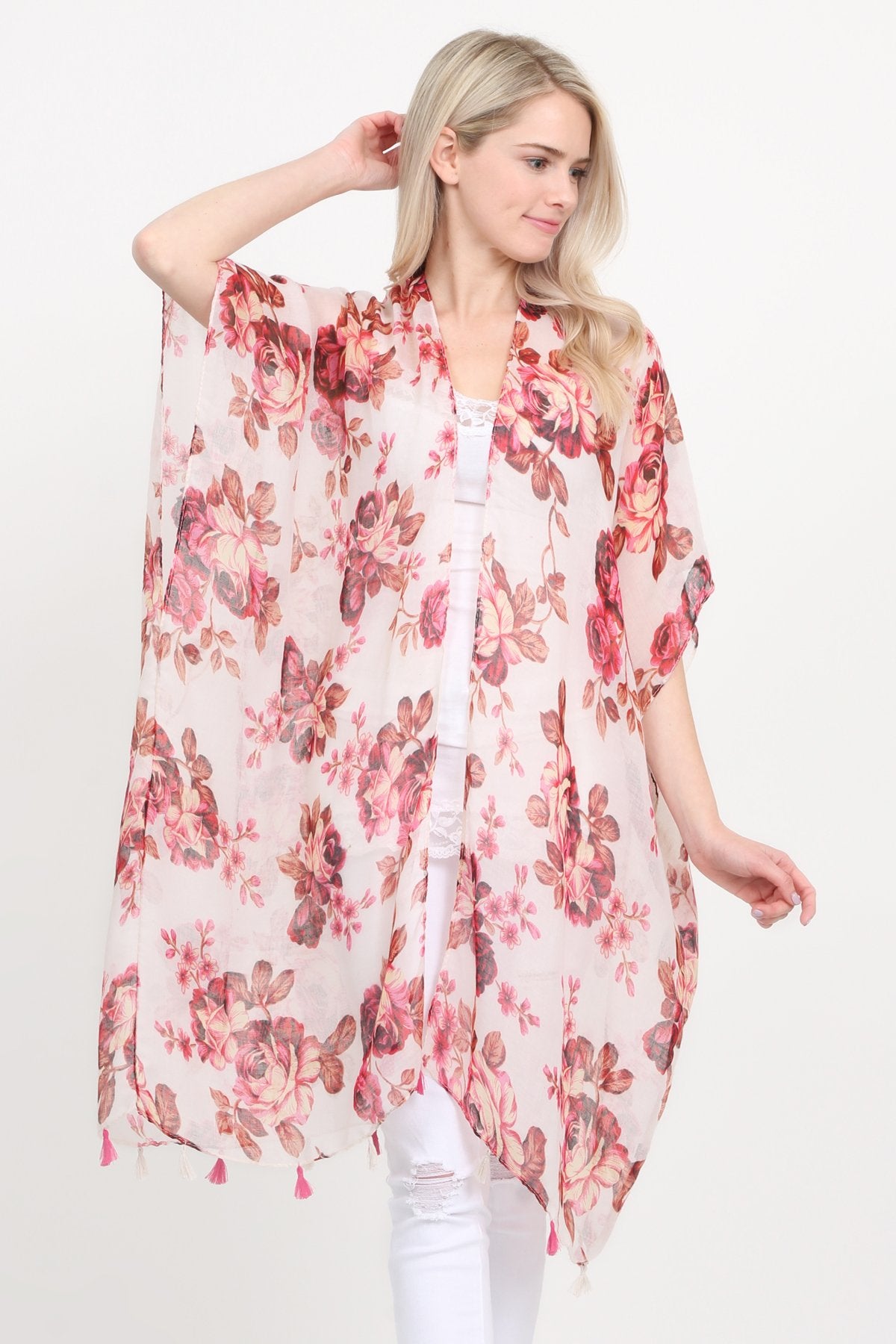 A woman stands against a plain background, wearing a Riah Fashion beige blue open front knee-length floral cardigan over a white outfit.