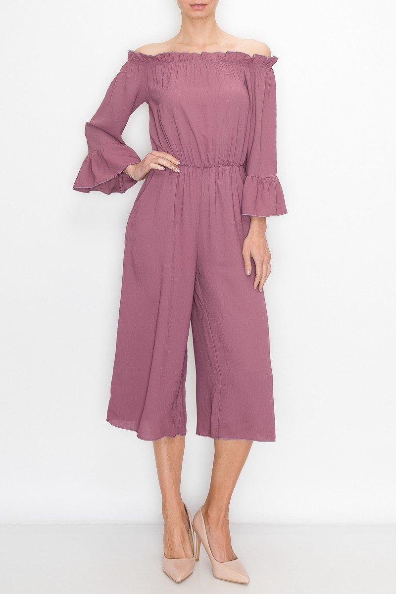 A person in a Stylespect Off Shoulder Jumpsuit - Mauve with bell sleeves and neutral heels poses against a plain white background.