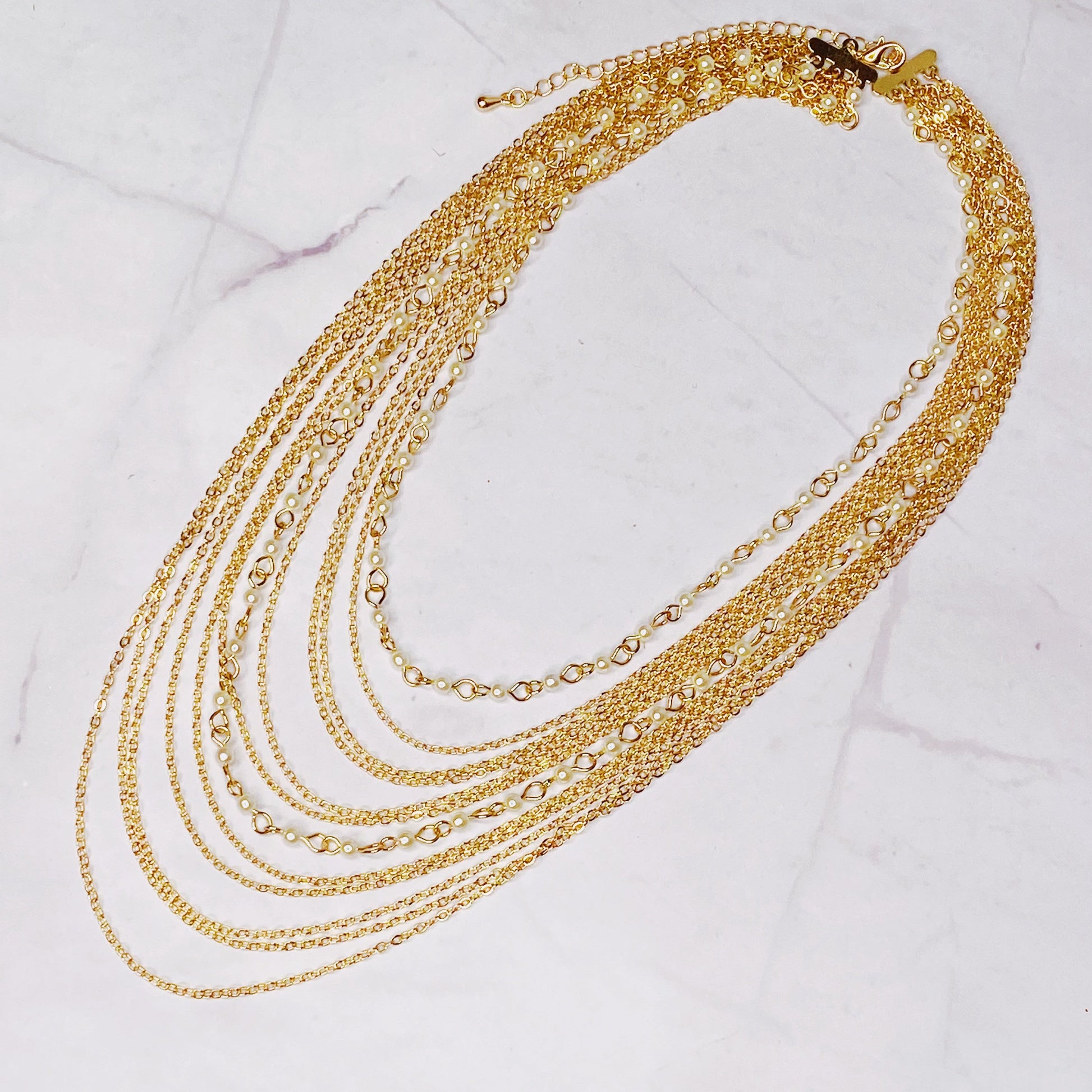 The Beautifully Draping Pearl and Chain Necklace by Ellison + Young is elegantly displayed on a white surface, showcasing its intricate chain designs.