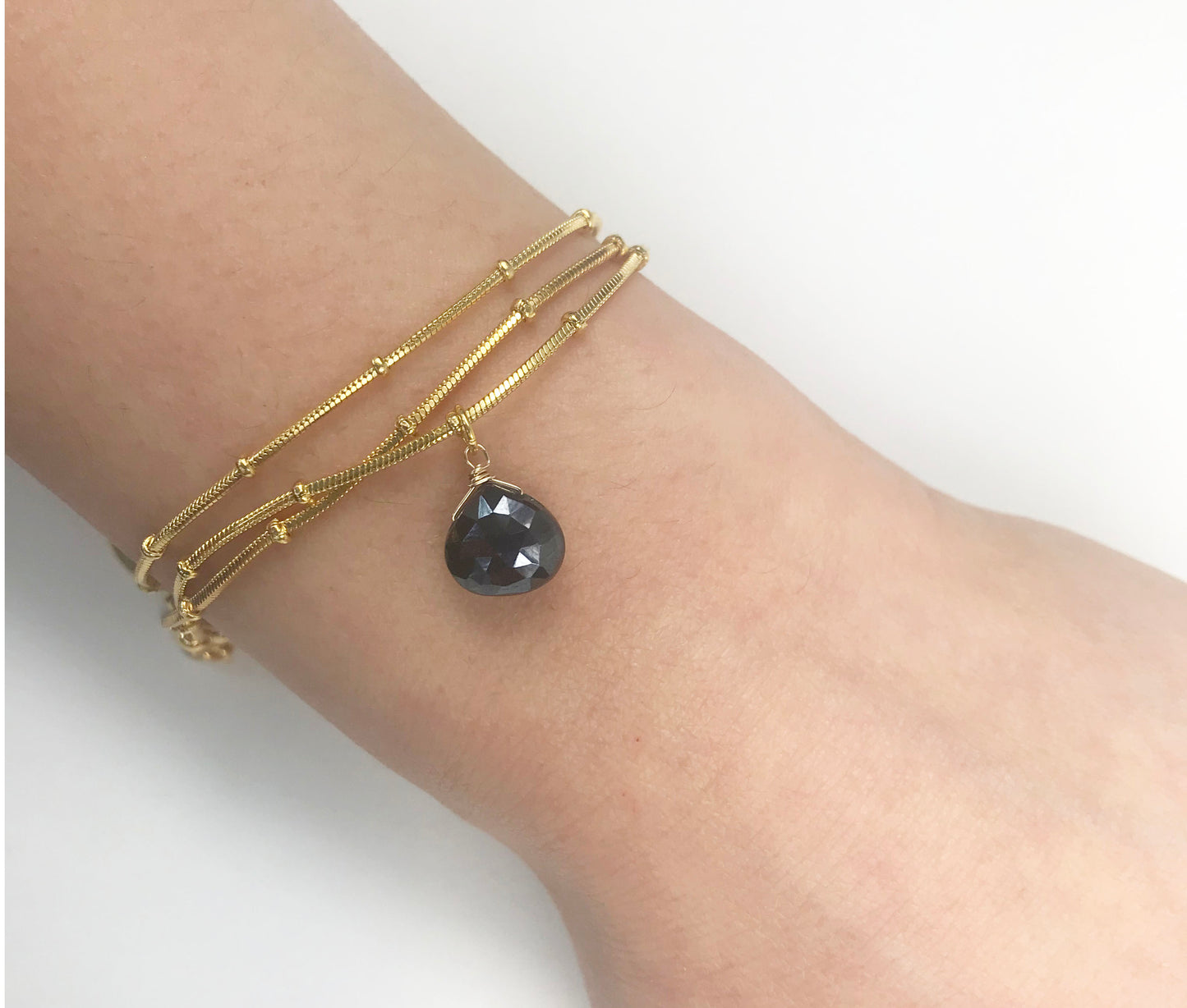 Gena Myints Black Spinel Drop Ball Chain Bracelet features an adjustable gold chain, a small black spinel pendant, and a branded charm.