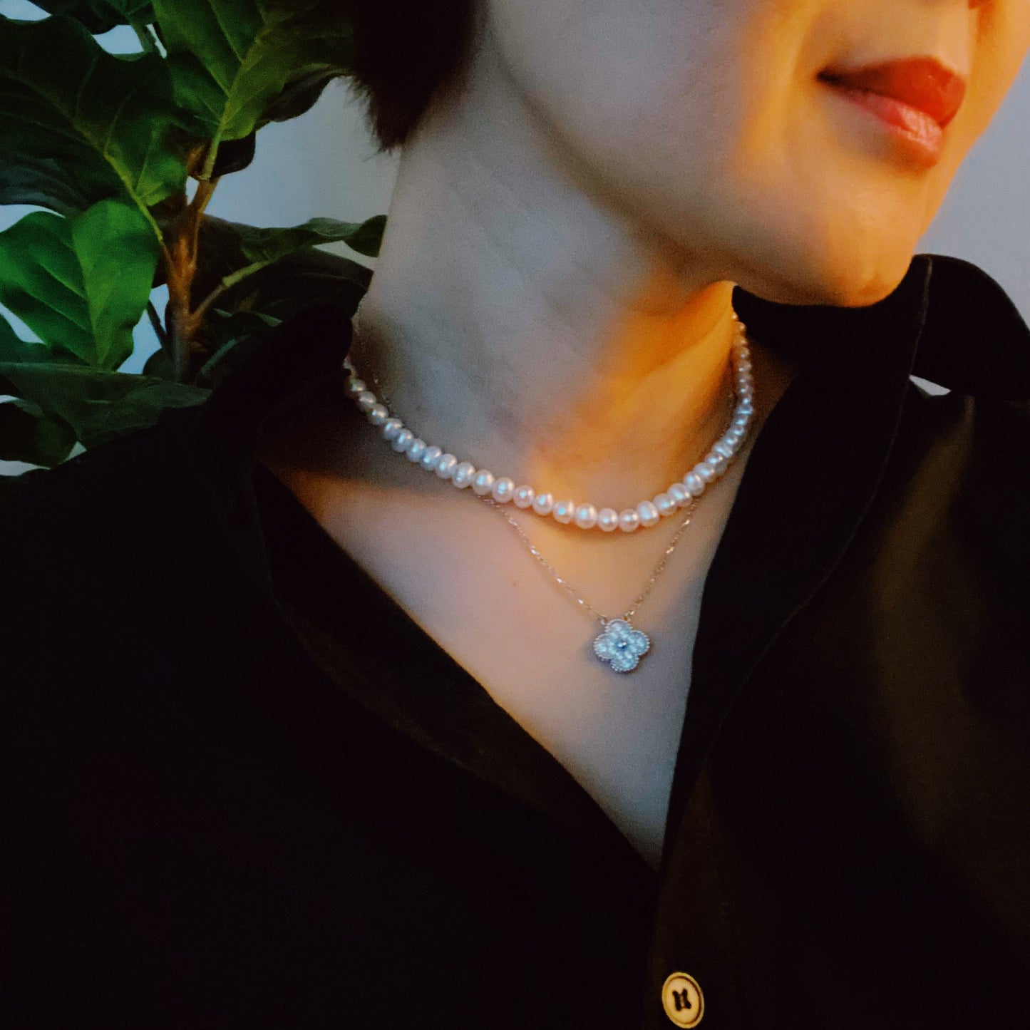 The Clover Clasp Genuine Pearl Necklace by Ellison + Young features rows of round white pearls elegantly displayed on a light surface.