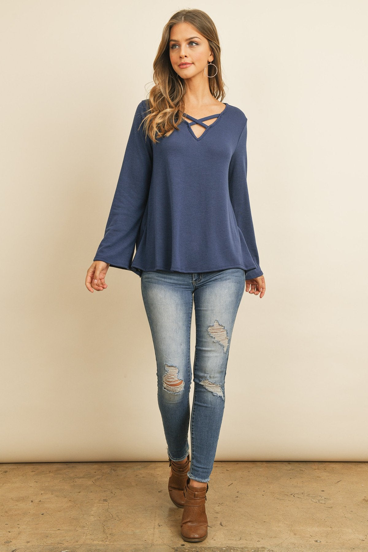 A person wearing a Riah Fashion Criss Cross Neck Long Sleeve Hacci Top in Dusty Blush and blue jeans stands against a neutral background, smiling.