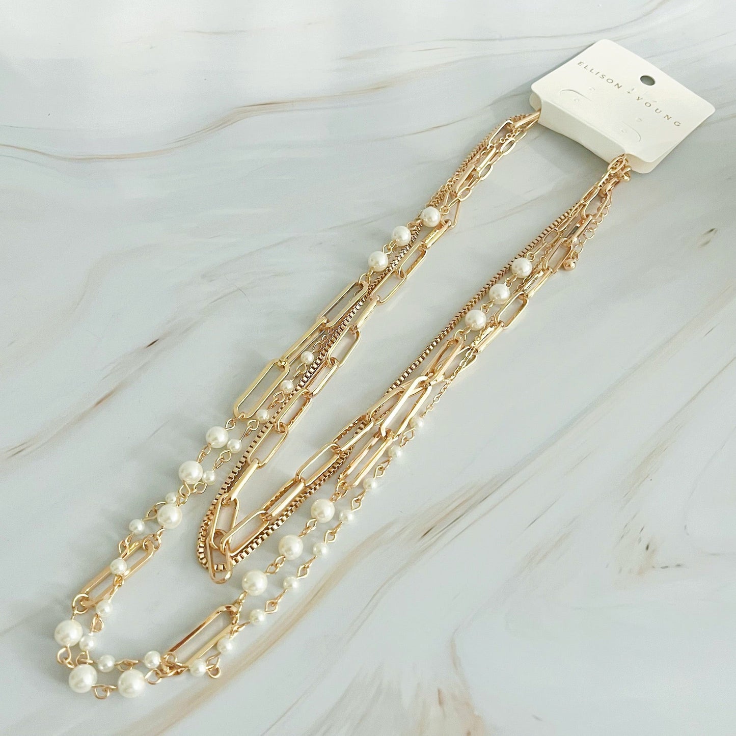 The Fourfect Layered Clip Chain Necklace by Ellison + Young displayed on a white marble surface.