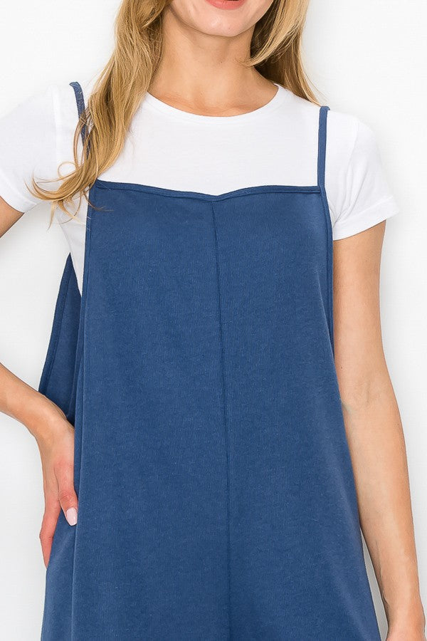 A person wearing a Stylespect Cropped Bottom Wide Leg Oversized Jumpsuit in blue over a white T-shirt and white sneakers, standing and smiling against a plain white background.