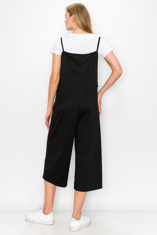 A person models the Stylespect Cropped Bottom Wide Leg Oversized Jumpsuit in black, paired with a white t-shirt and white sneakers, set against a plain white backdrop.