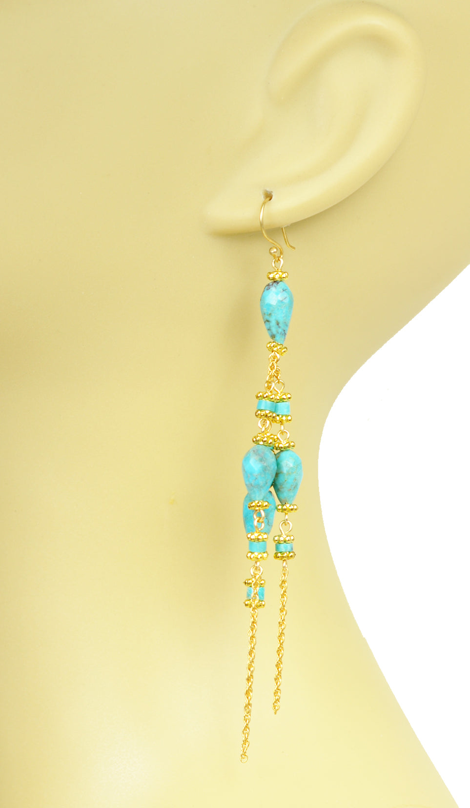 Gena Myints Turquoise Linear Chandelier Earrings feature turquoise stones, gold accents, and chain tassels.