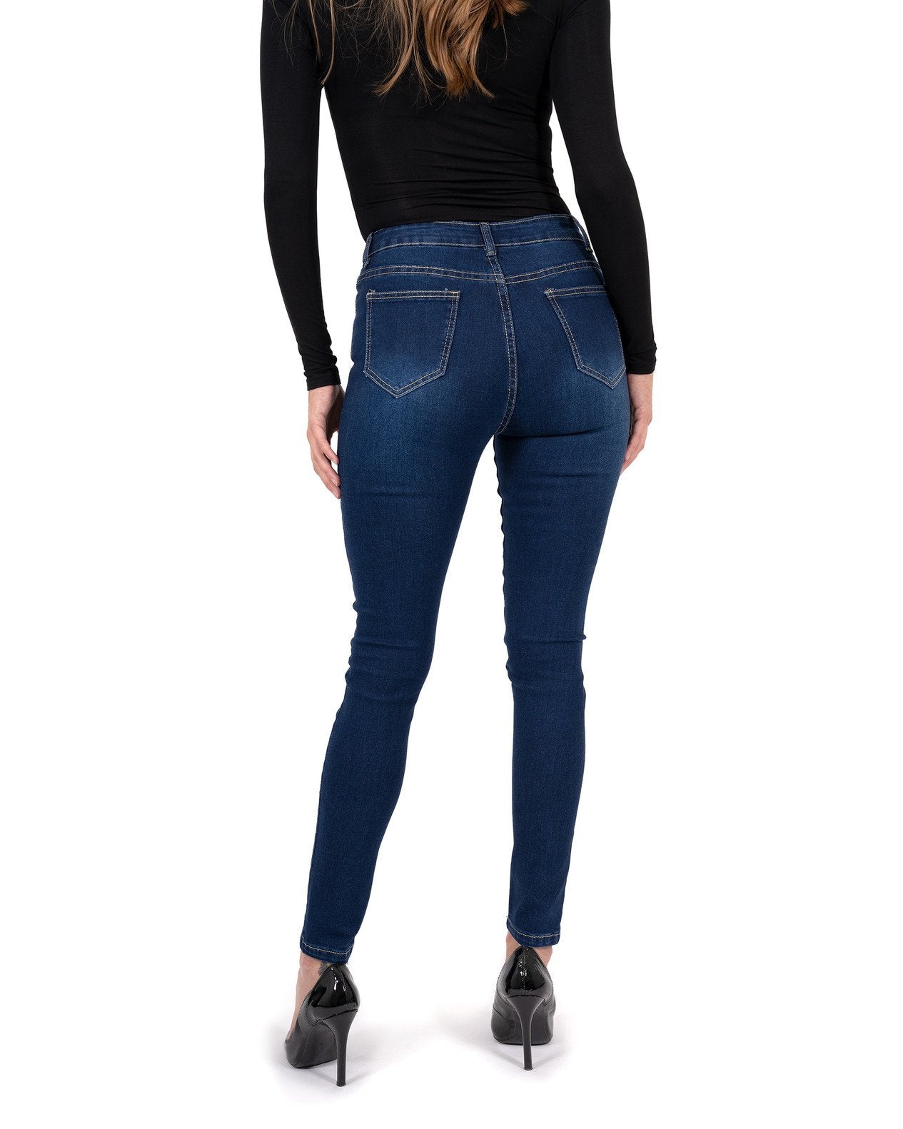A person stands by a pool wearing a black long-sleeve shirt, Alexis High Waist Skinny Jeans by Savoy Active, and heels. Tall trees and vibrant flowers surround the area.