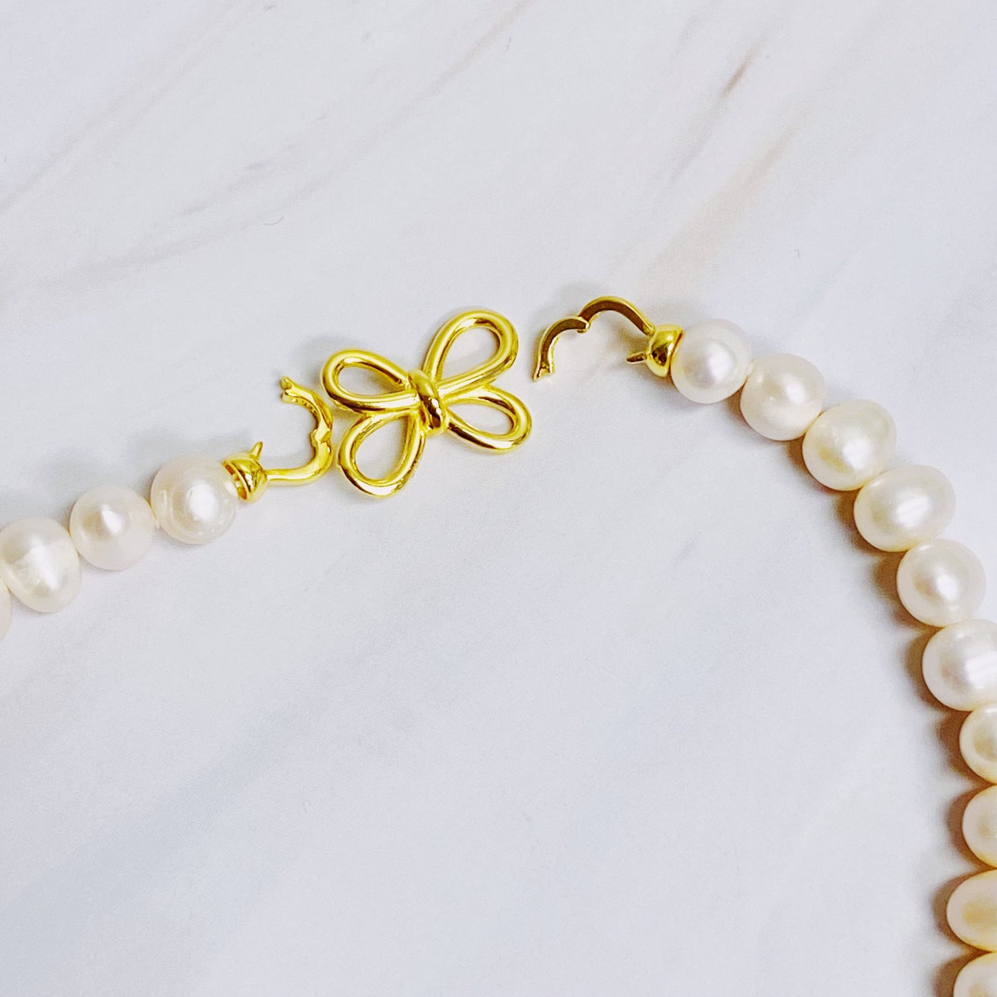 The Clover Clasp Genuine Pearl Necklace by Ellison + Young features rows of round white pearls elegantly displayed on a light surface.