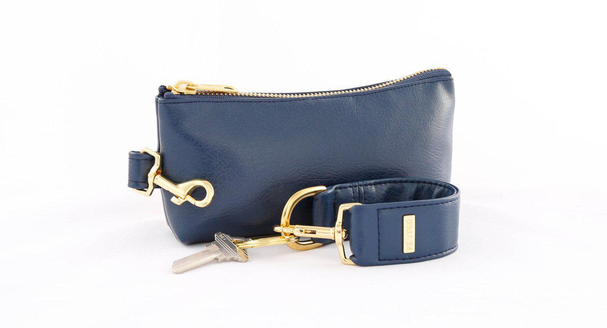 A compact True Navy vegan leather bag by KEYPER, with a gold zipper and clasp, comes with a detachable strap and includes a silver key attached to a key ring. Part of the 2-piece wristlet set.
