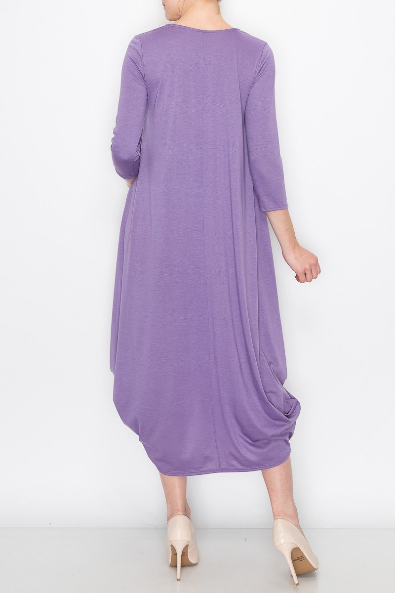 A person models the Stylespect Solid Balloon Dress in purple with its long sleeves and asymmetrical cut, paired with beige heels, all set against a plain white background.