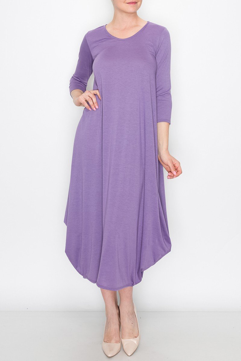 A person models the Stylespect Solid Balloon Dress in purple with its long sleeves and asymmetrical cut, paired with beige heels, all set against a plain white background.