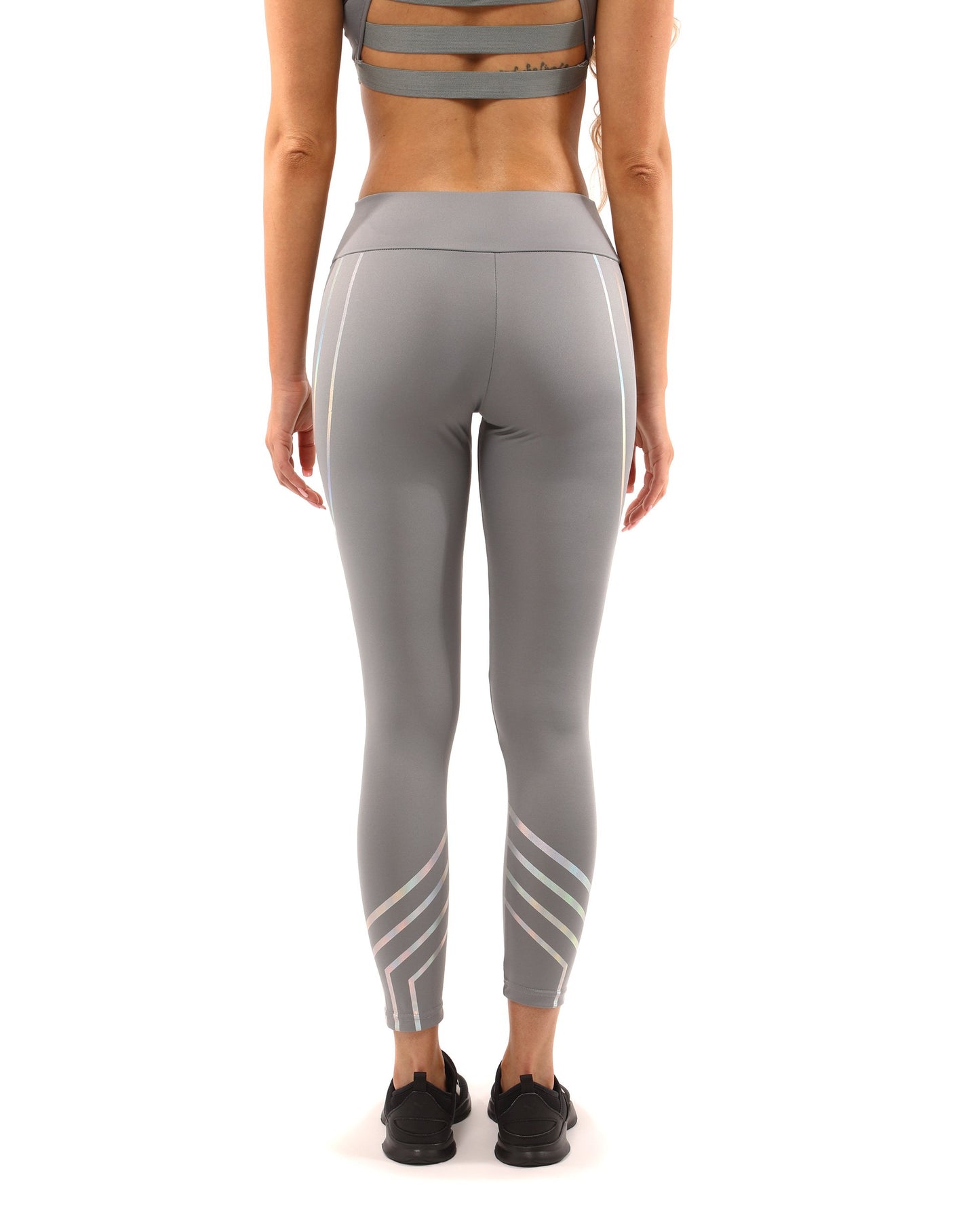 A woman in Savoy Actives grey Laguna Leggings stands on outdoor steps, adjusting her top while facing away from the camera.