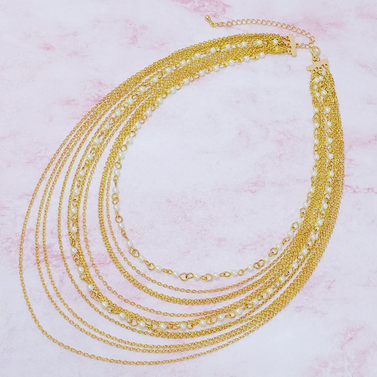 The Beautifully Draping Pearl and Chain Necklace by Ellison + Young is elegantly displayed on a white surface, showcasing its intricate chain designs.