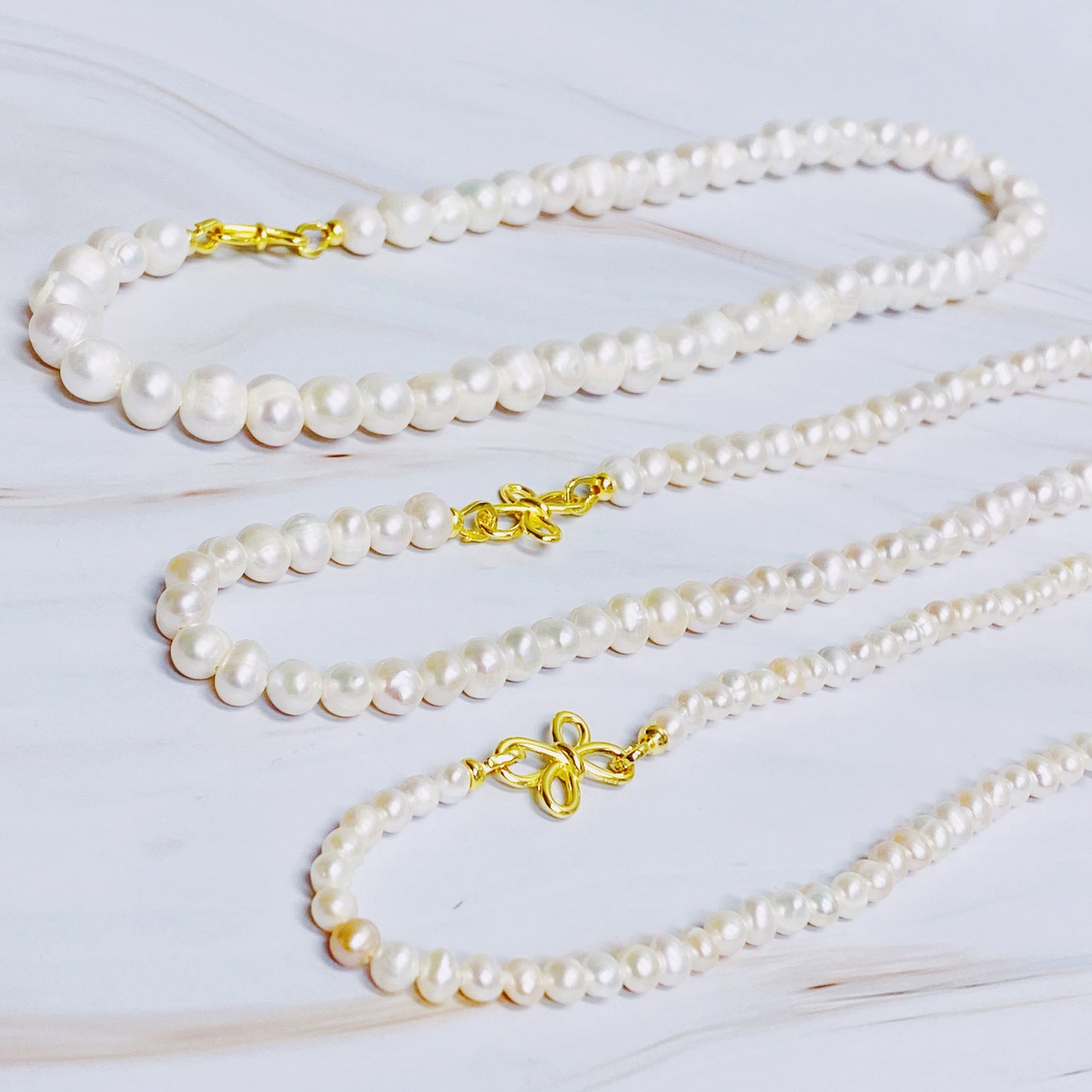 The Clover Clasp Genuine Pearl Necklace by Ellison + Young features rows of round white pearls elegantly displayed on a light surface.