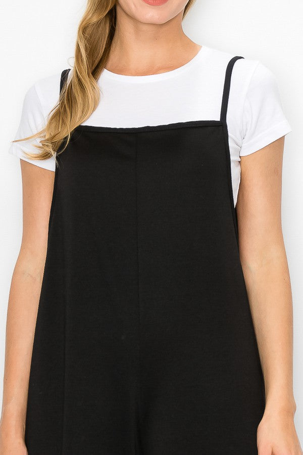 A person models the Stylespect Cropped Bottom Wide Leg Oversized Jumpsuit in black, paired with a white t-shirt and white sneakers, set against a plain white backdrop.