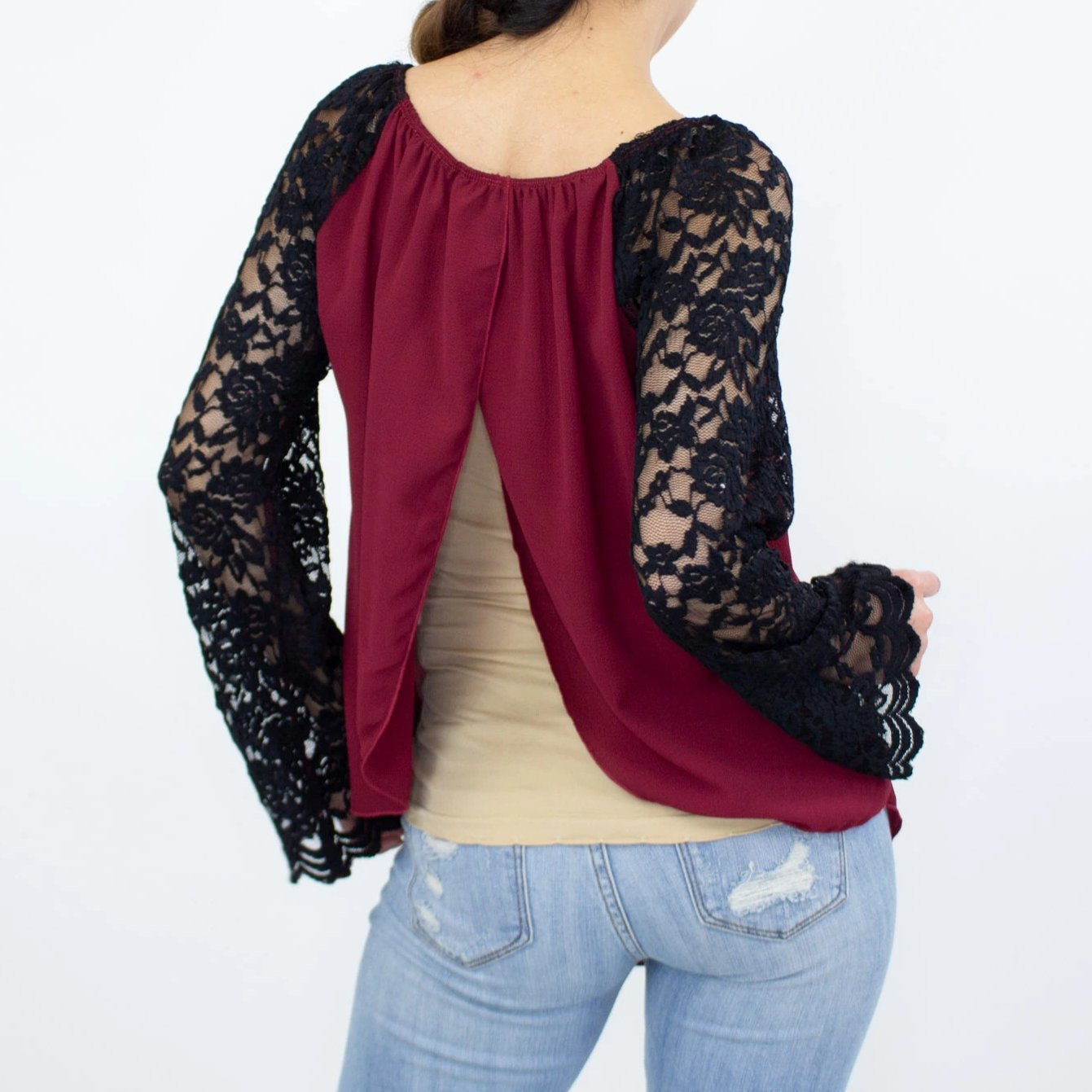 A person wearing a Stylespect Lace Sleeve Backless Top in burgundy and ripped jeans, standing against a plain white background.