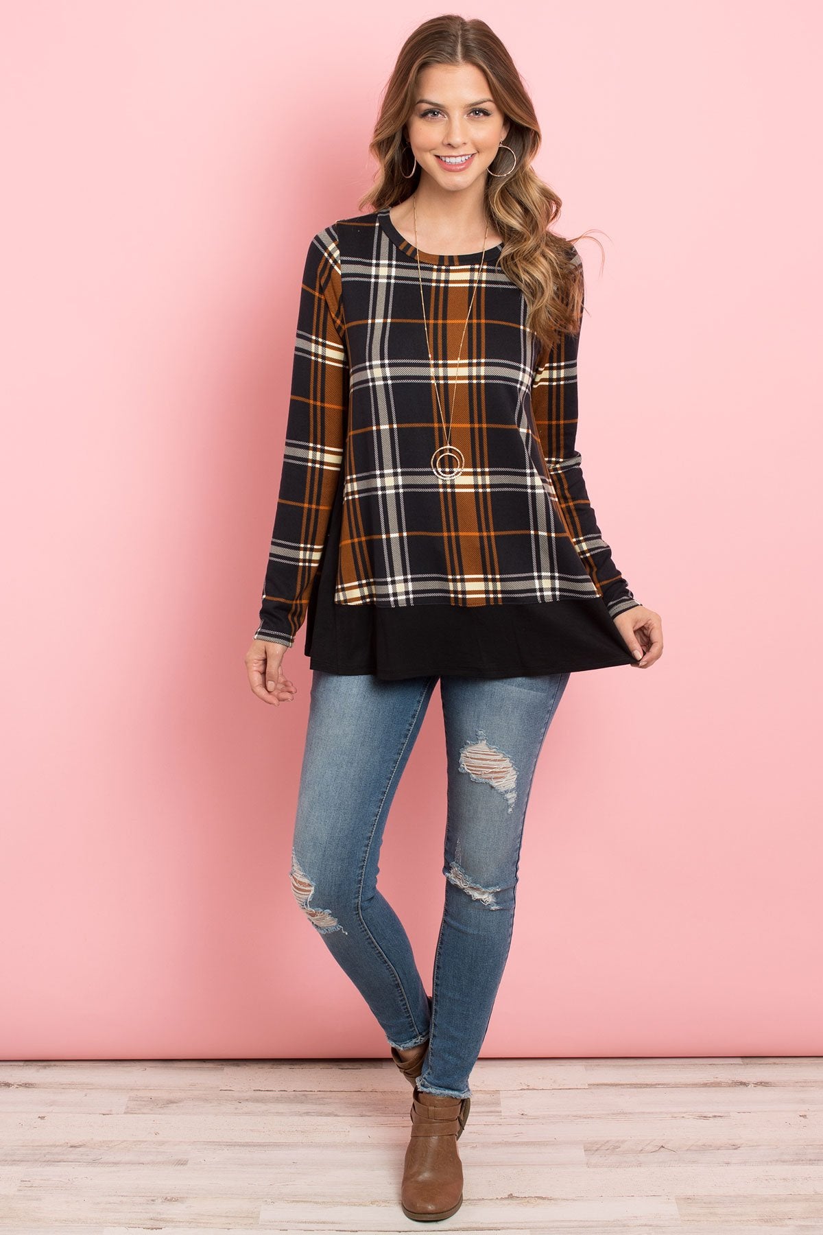 A person in a Riah Fashion Solid Hem and Side Contrast Plaid Top in Navy Black, paired with ripped jeans, stands against a pink background.