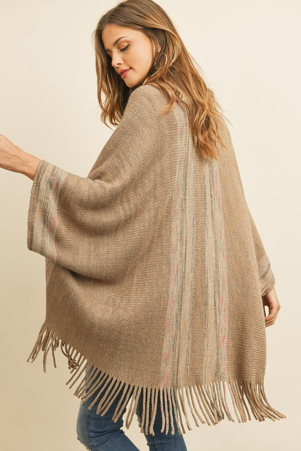 Someone is wearing a Fringe Stripe Open Front Kimono by Riah Fashion over a beige top and ripped jeans, standing against a plain background.