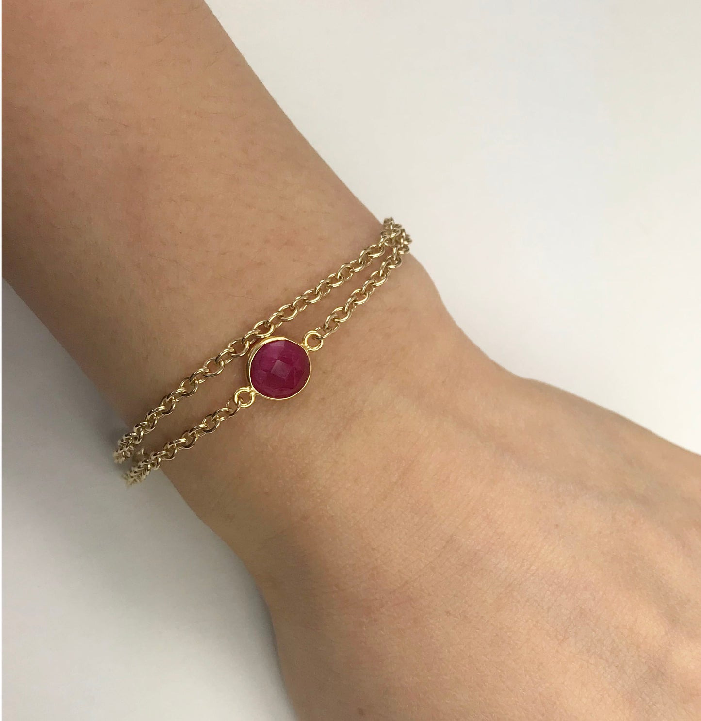 The Gena Myint Ruby Vermeil Double Chain Bracelet features a pink gemstone centerpiece, an adjustable clasp, and a small heart charm.