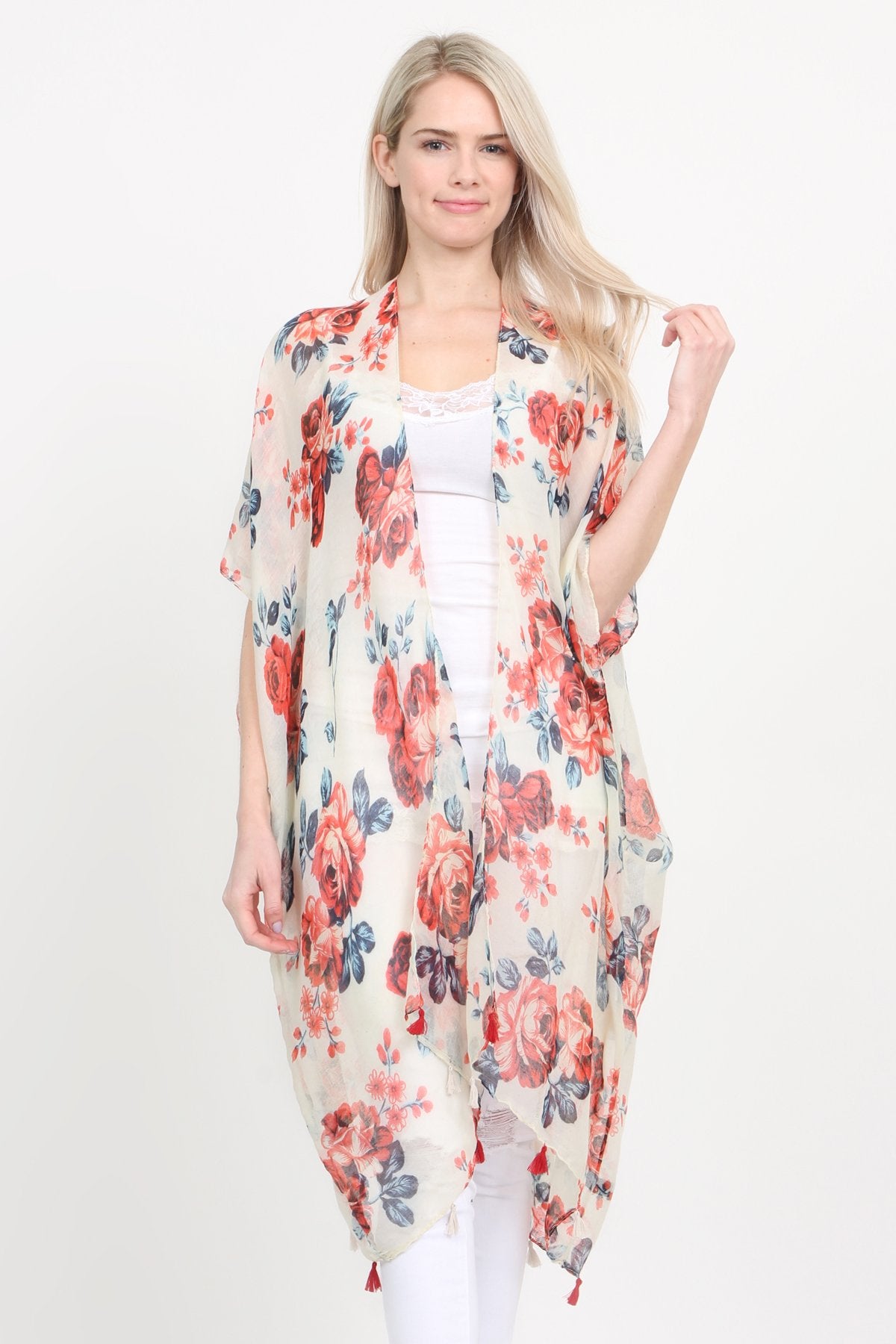 A woman stands against a plain background, wearing a Riah Fashion beige blue open front knee-length floral cardigan over a white outfit.