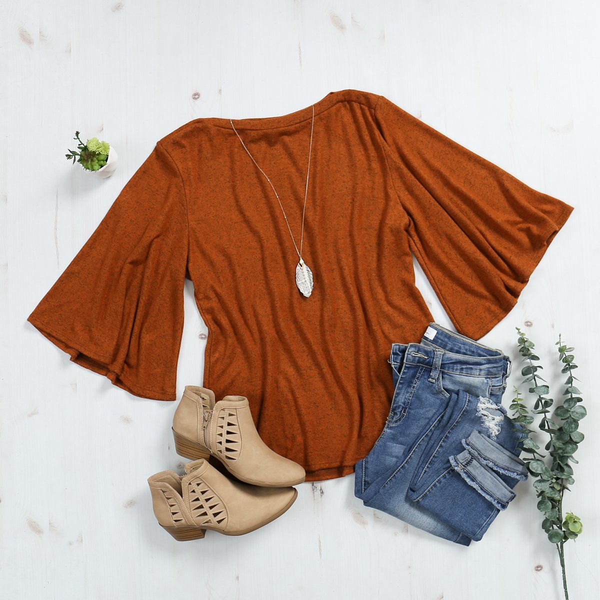 A person in a Riah Fashion Boat Neck Bell Sleeve Solid Hacci Brushed Top and ripped jeans stands against a neutral background, accessorized with hoop earrings and a long necklace.