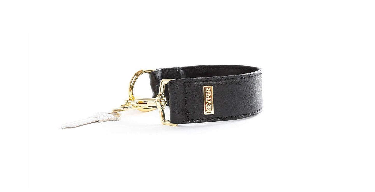 A Classic Black PREMIUM LEATHER KEYPER® key ring features a black leather bracelet with a gold clasp and branded KEYPER tag, attached to a key.