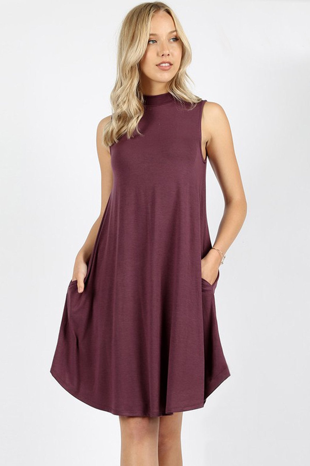 A woman is wearing the Riah Fashion Premium Mock Neck Sleeveless Dress with pockets in maroon, with her right hand in a pocket.