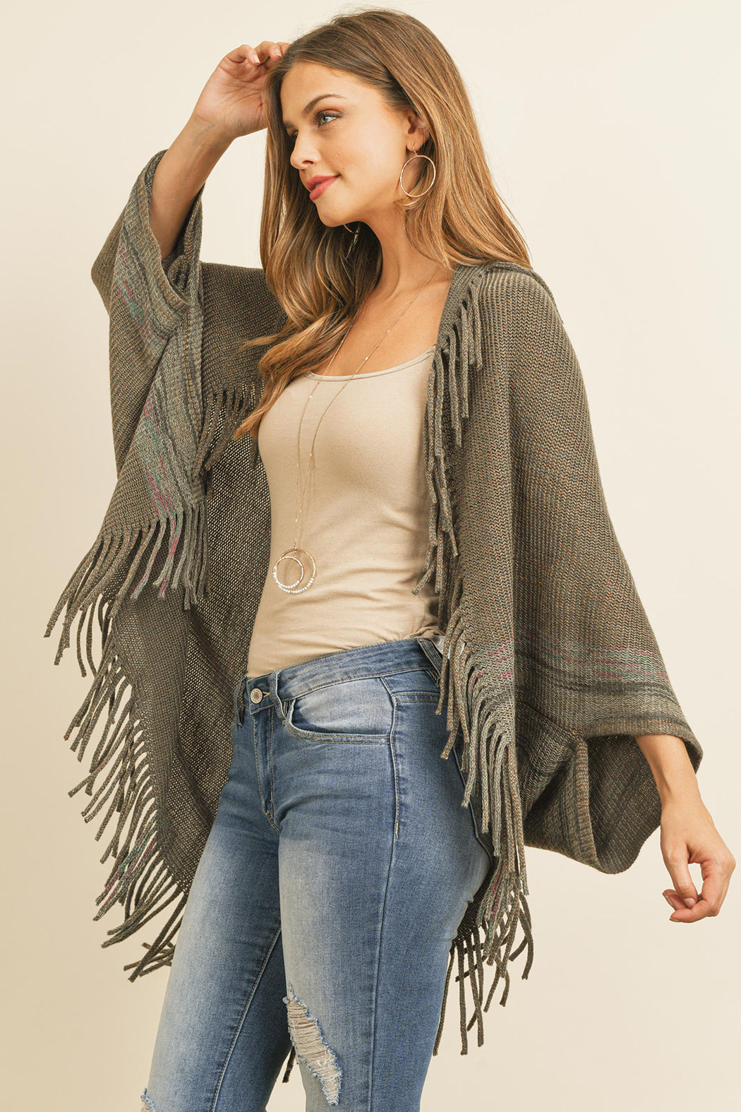 Someone is wearing a Fringe Stripe Open Front Kimono by Riah Fashion over a beige top and ripped jeans, standing against a plain background.