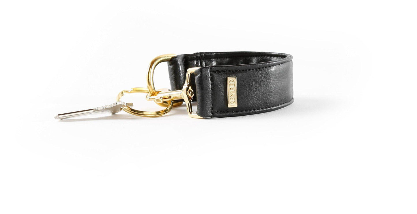 The Classic Black Vegan Leather KEYPER® Key Ring by KEYPER features a black leather wristband with a gold keyring that holds two keys.
