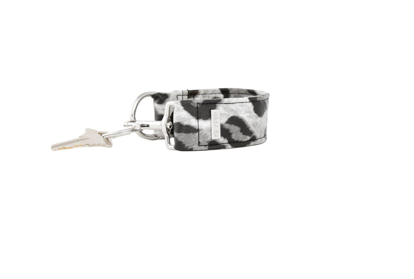 The KEYPER brands Snow Leopard Vegan Leather KEYPER® Key Ring features a leopard print design, a gold key ring with an attached key, and a small rectangular gold label.