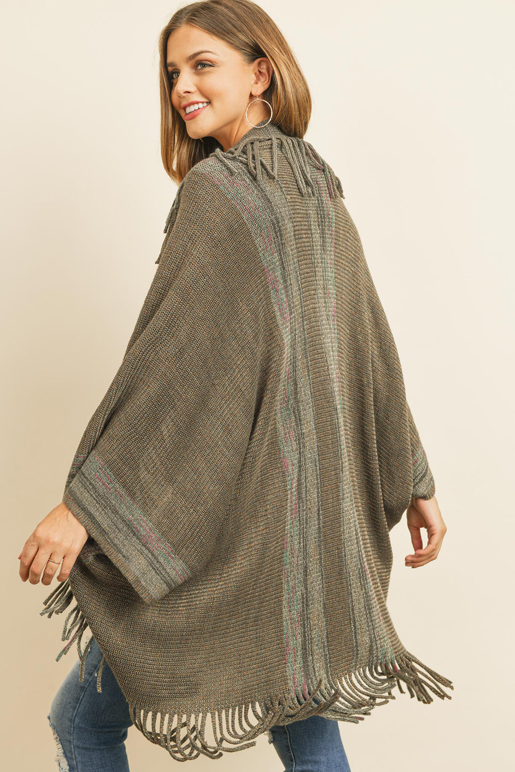 Someone is wearing a Fringe Stripe Open Front Kimono by Riah Fashion over a beige top and ripped jeans, standing against a plain background.