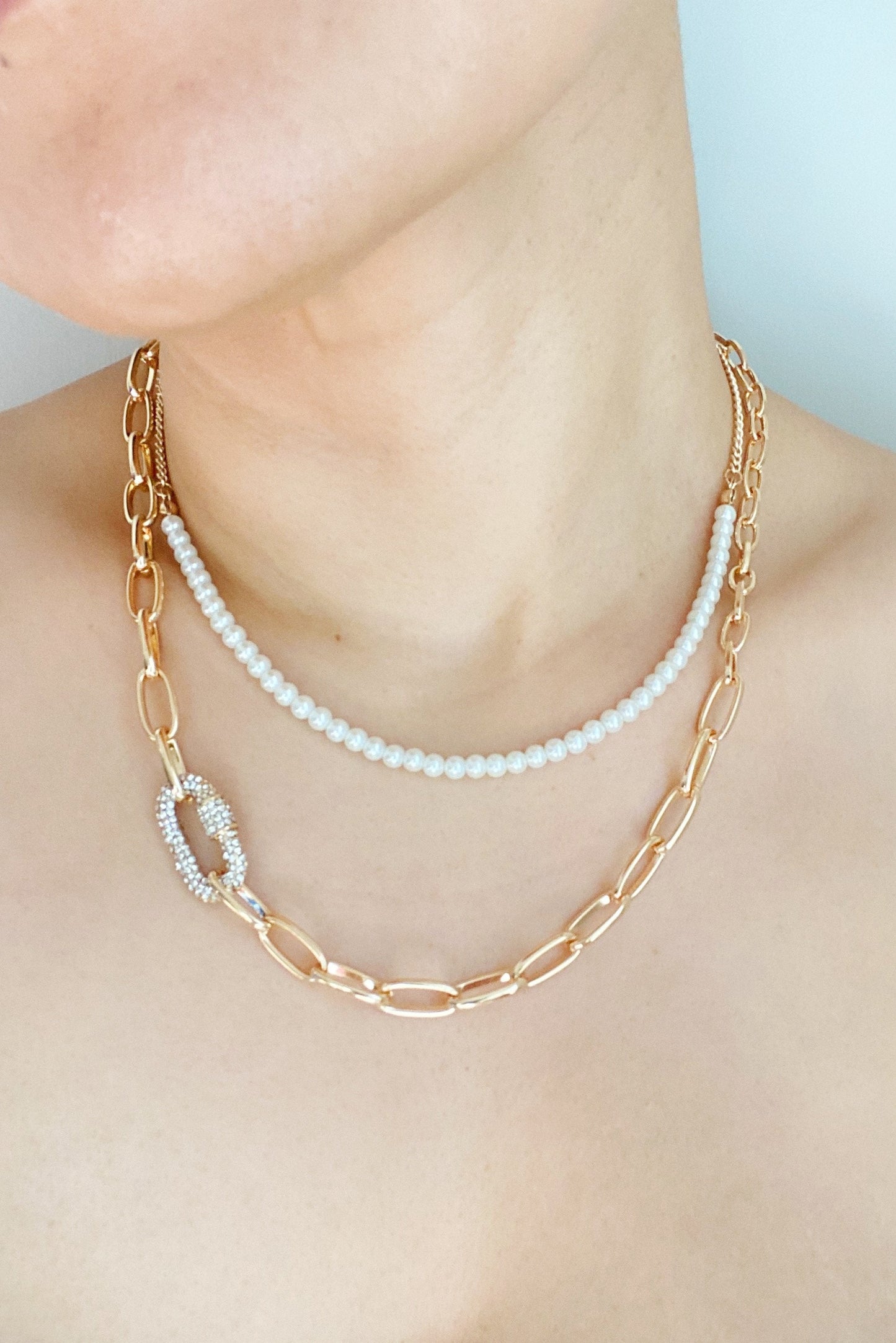 A person wearing the Ellison + Young Classic Duo Layered Pearl Necklace Set with gold links and pearl accents, plus a simple strand of pearls.