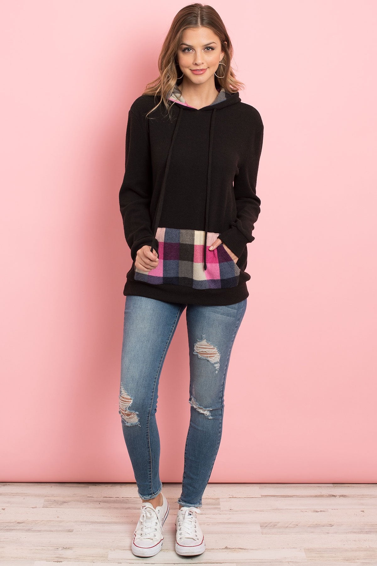 Someone wearing the Riah Fashion Hacci Brushed Plaid Kangaroo Pocket Hoodie stands indoors with plants in the background.