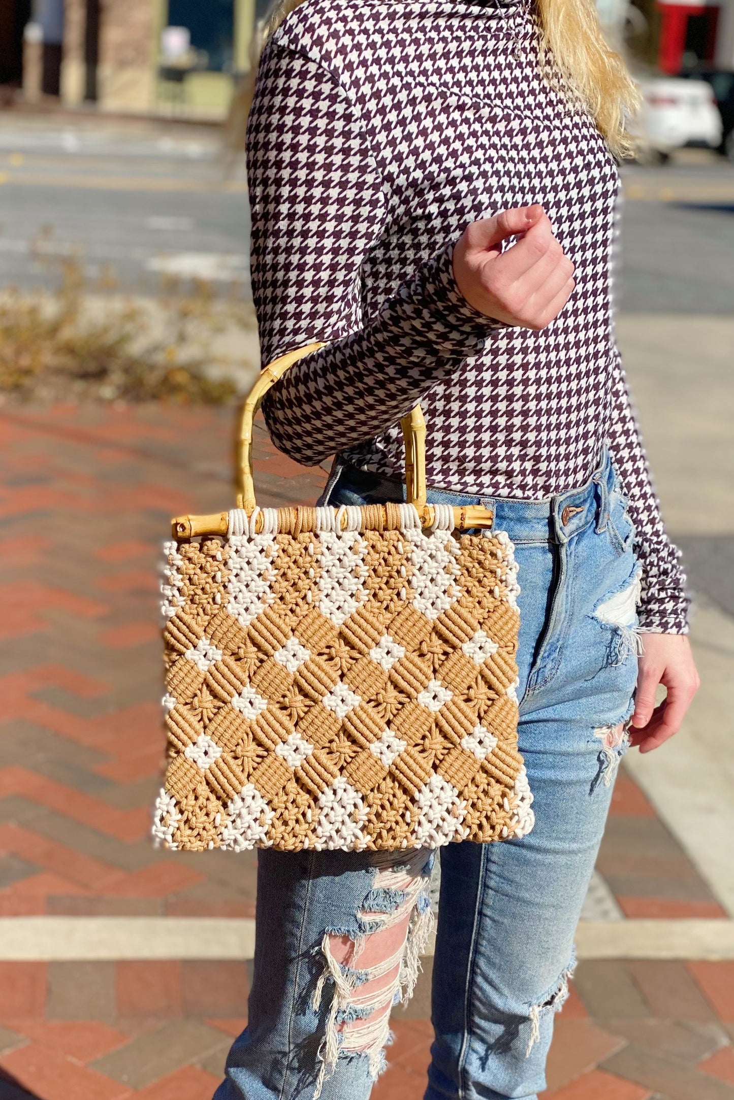 A person holds the Ellison + Young Bamboo Babe Tote, wearing a houndstooth shirt and ripped jeans. The background features a paved walkway and street.