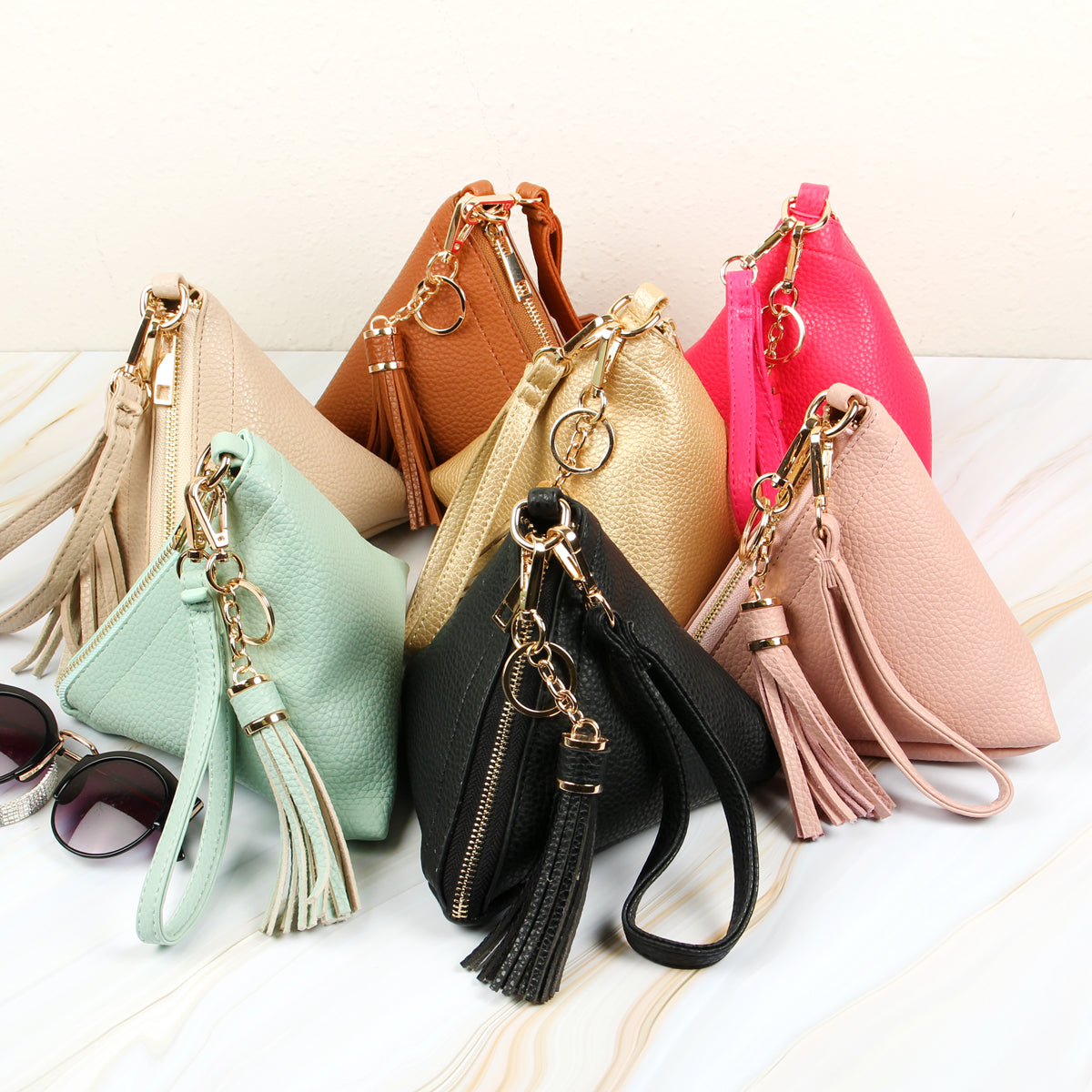 A person in a white shirt and jeans is holding the Riah Fashion Pyramid Shape Tassel Wristlet Leather Bag in orange.