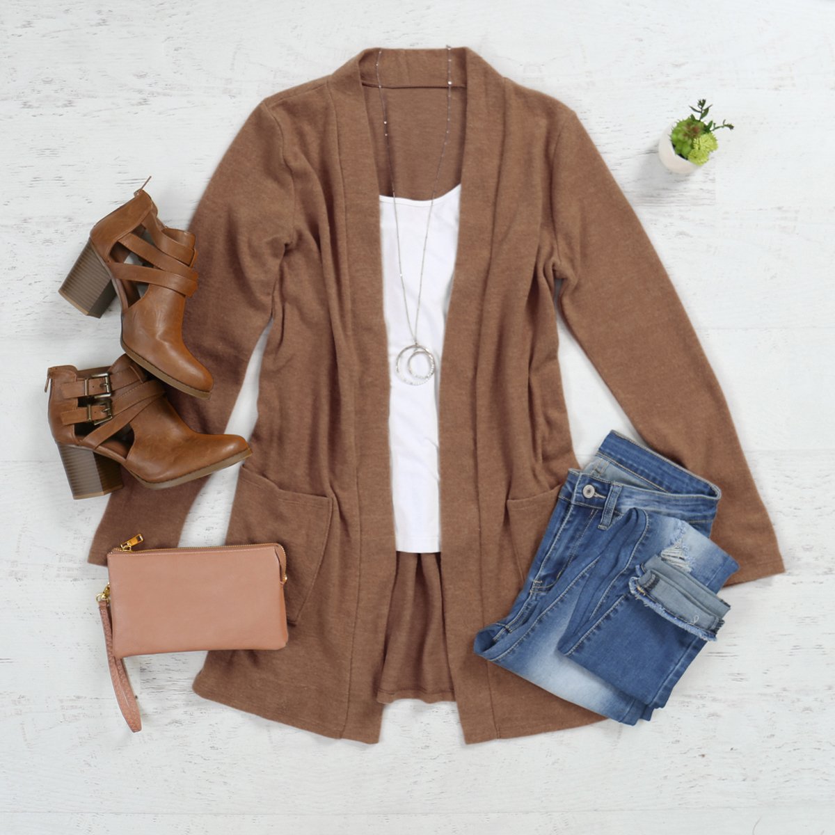 A woman in a Brushed Melange Open Front Cardigan by Riah Fashion and ripped jeans stands against a pink background, hands in her pockets.