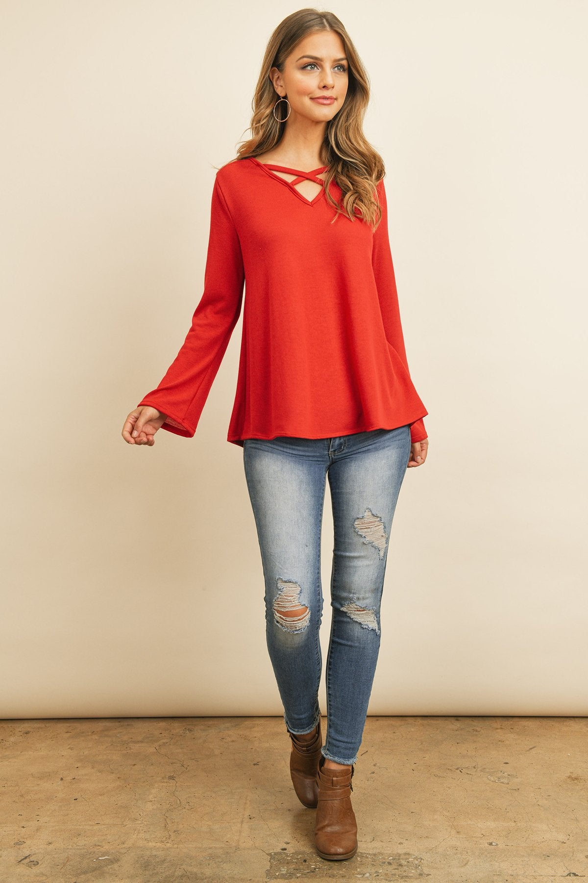 A person wearing a Riah Fashion Criss Cross Neck Long Sleeve Hacci Top in Dusty Blush and blue jeans stands against a neutral background, smiling.