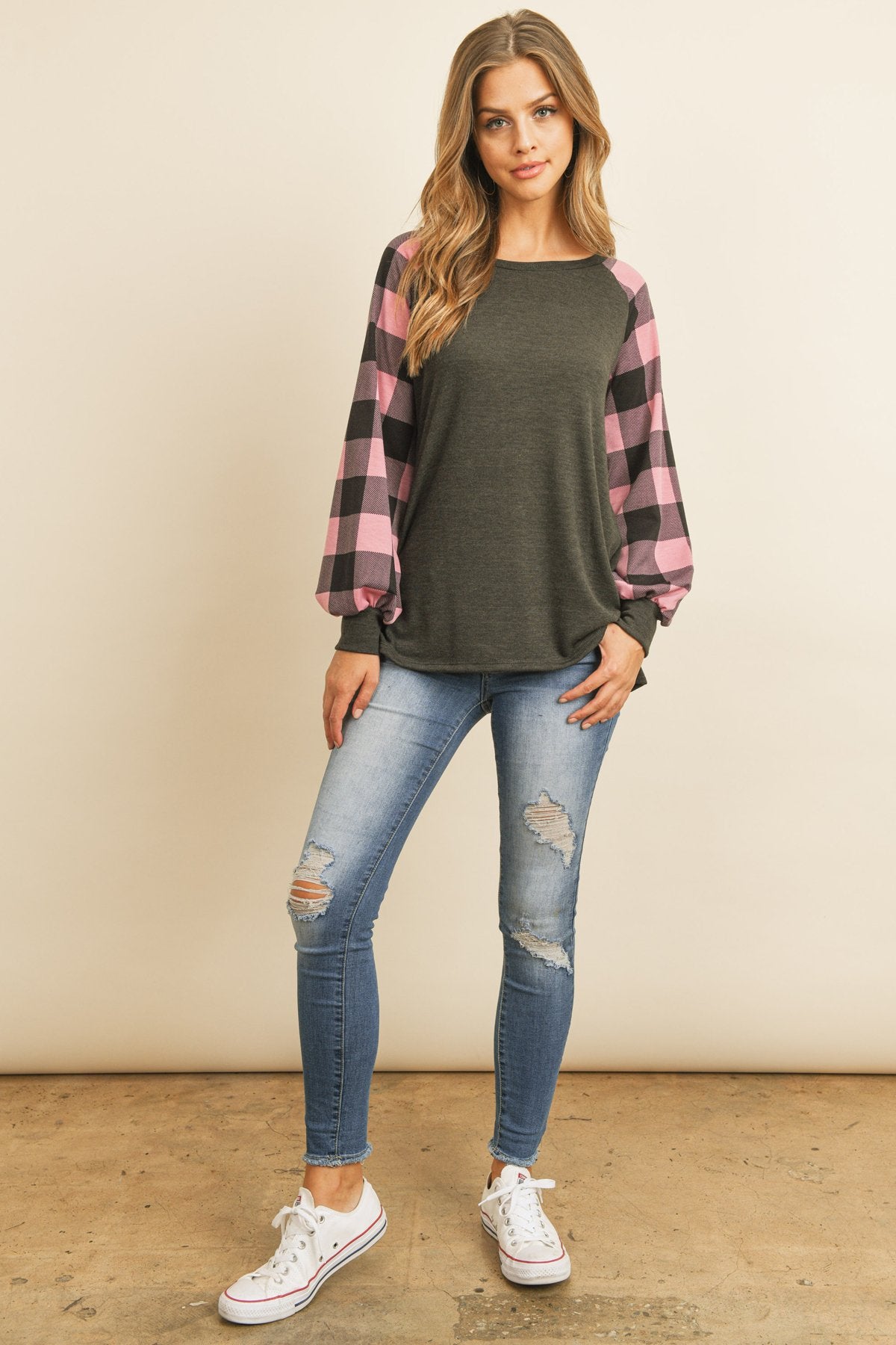 A woman wearing a faded denim plaid puff sleeved round neck top by Riah Fashion and ripped jeans stands against a plain background.
