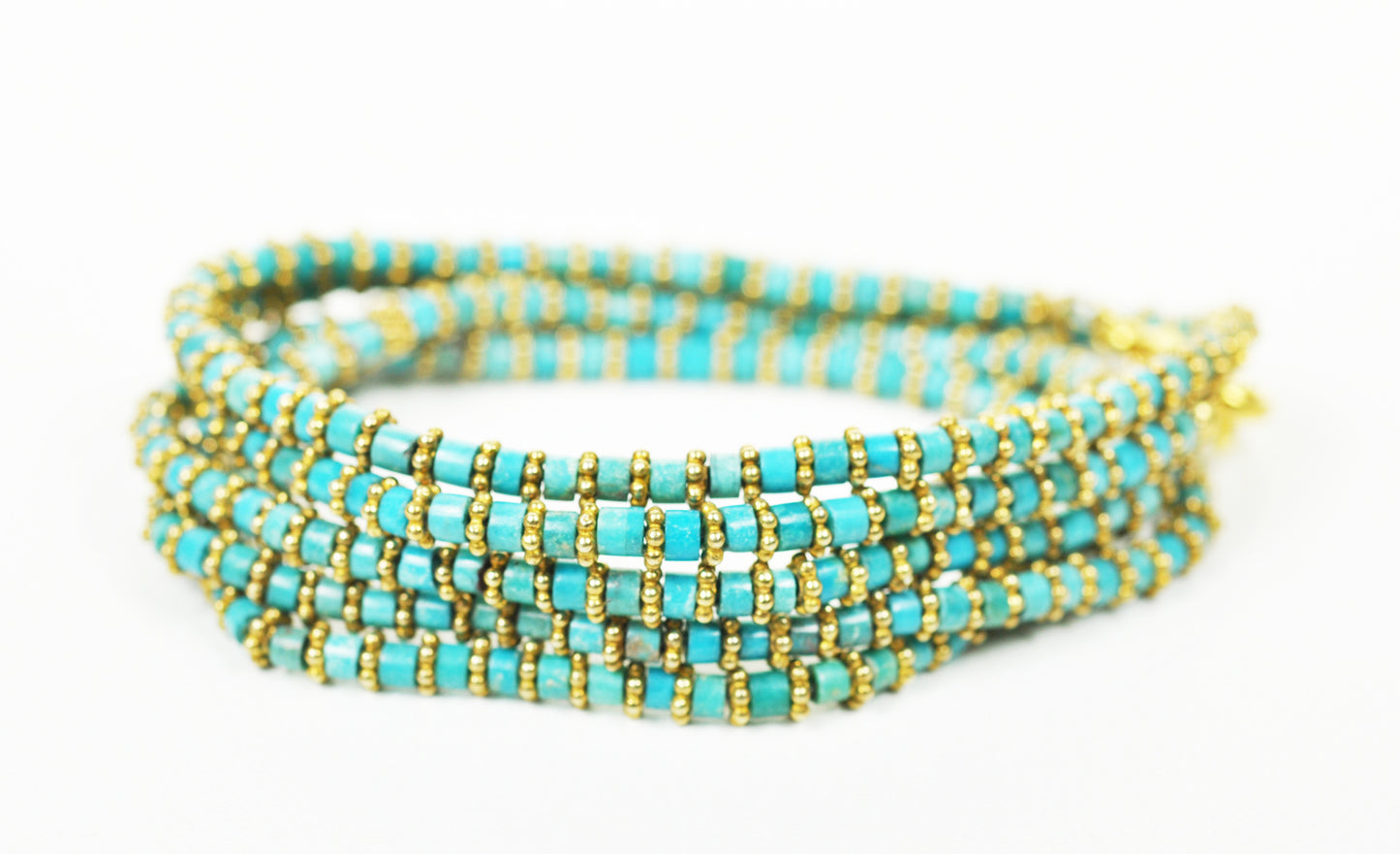 A Gena Myint Turquoise Wrap Bracelet with gold beads is set against a white background.