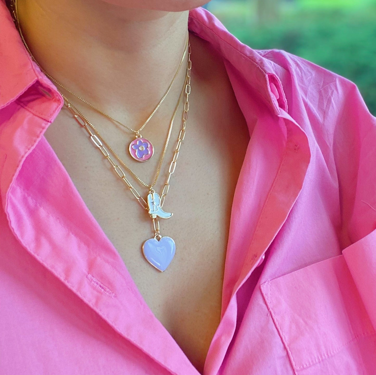 Two Cow Girl Boot Pendant Necklaces by Ellison + Young, one with a white boot and the other with a pink boot, are displayed on a marble surface.