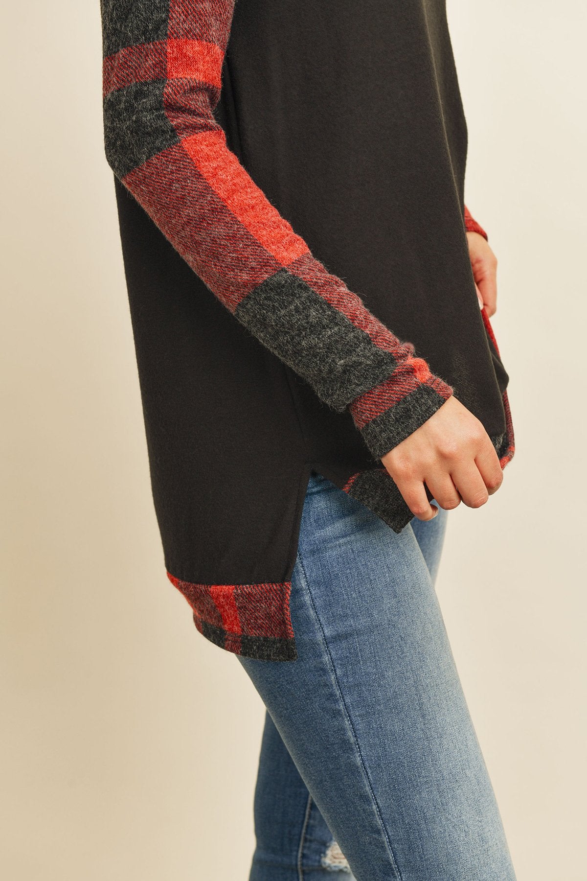 A woman in a Riah Fashion Brush Hacci Plaid Contrast Long Back Hem Top with red and beige accents, paired with blue ripped jeans, stands against a plain background.