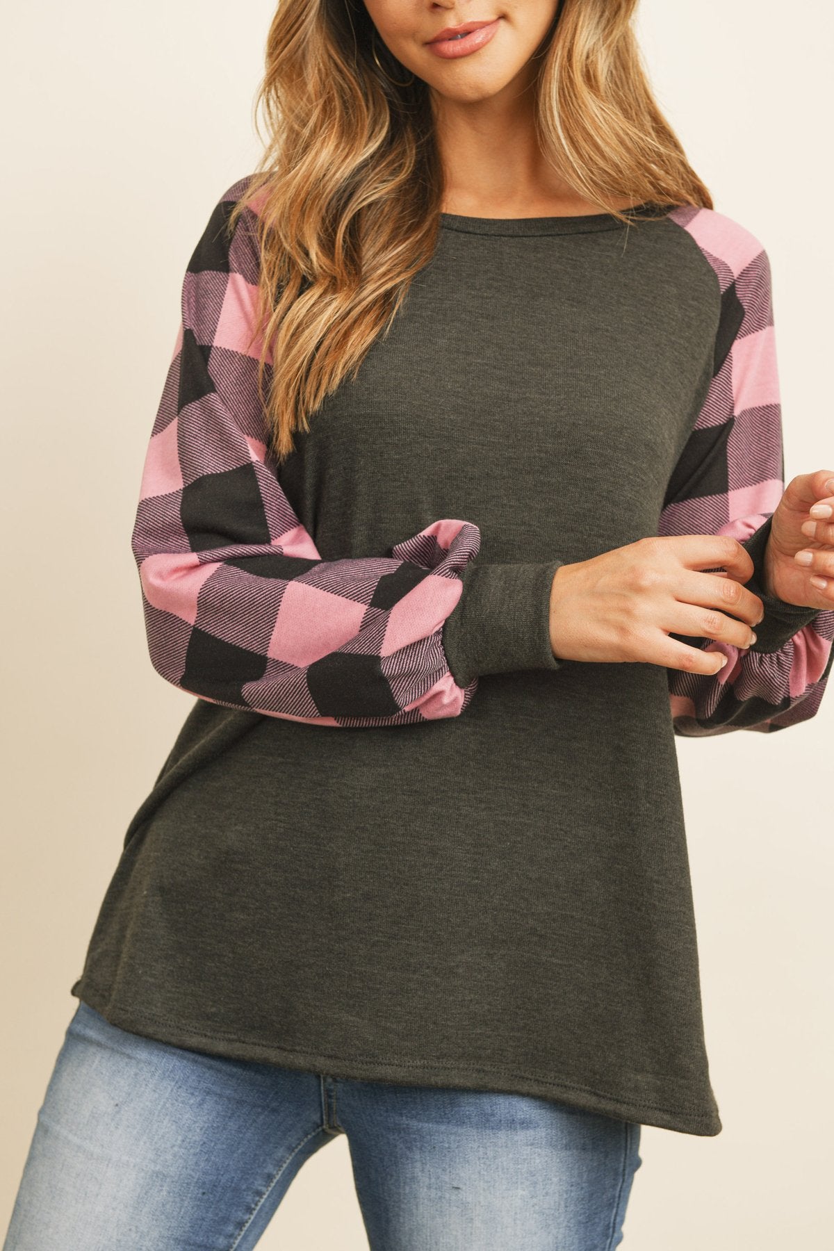 A woman wearing a faded denim plaid puff sleeved round neck top by Riah Fashion and ripped jeans stands against a plain background.