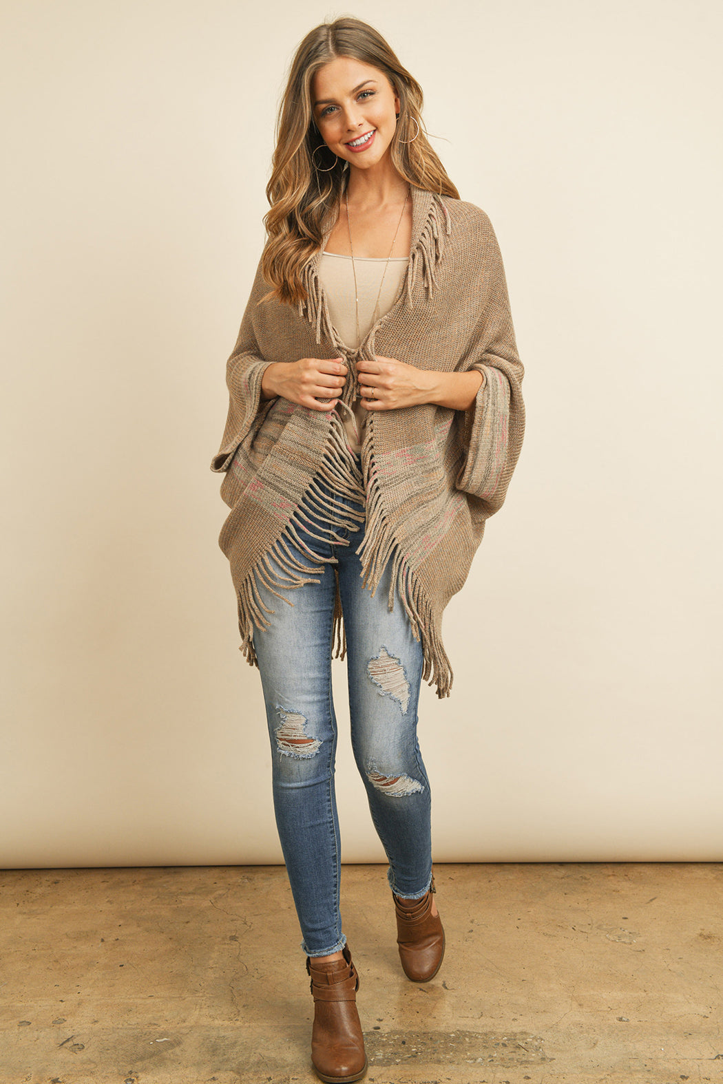 Someone is wearing a Fringe Stripe Open Front Kimono by Riah Fashion over a beige top and ripped jeans, standing against a plain background.