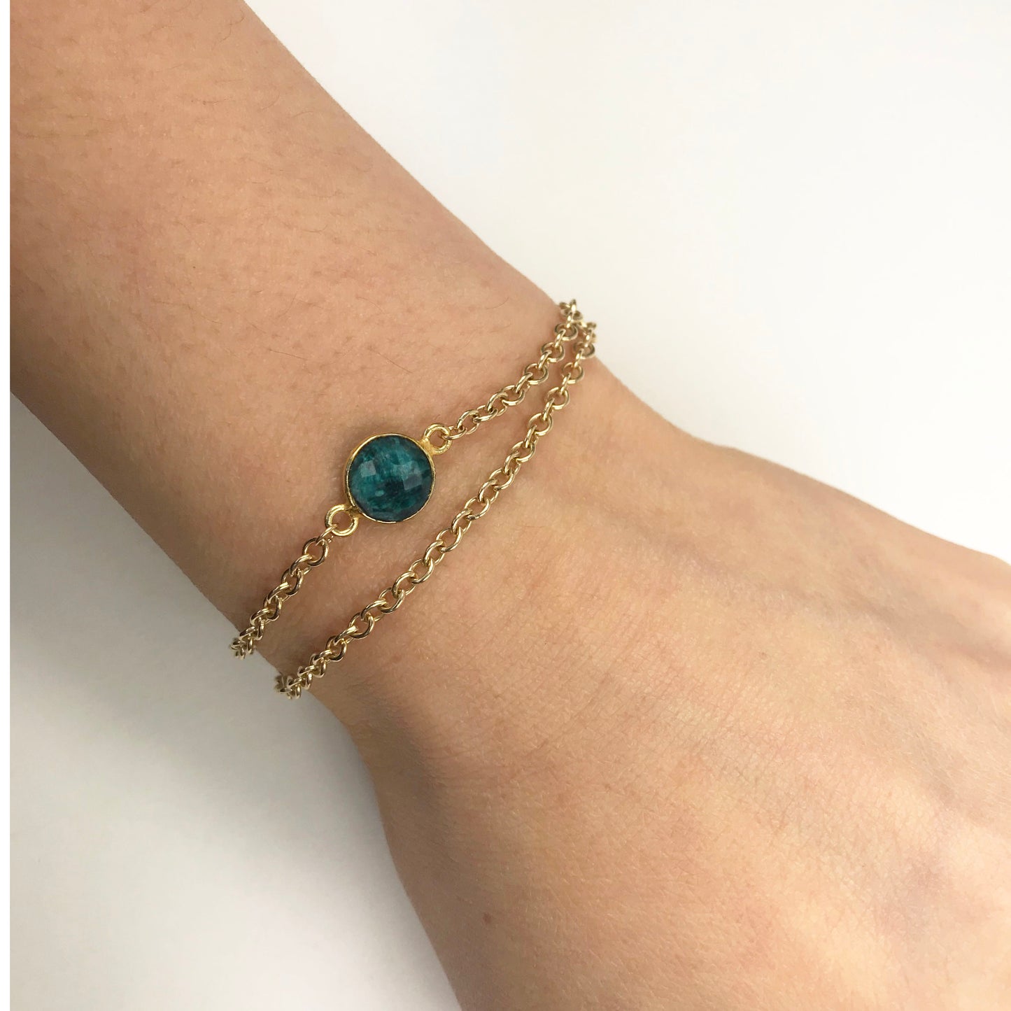 Gena Myints Emerald Vermeil Double Chain Bracelet features a central green stone and a heart-shaped charm.