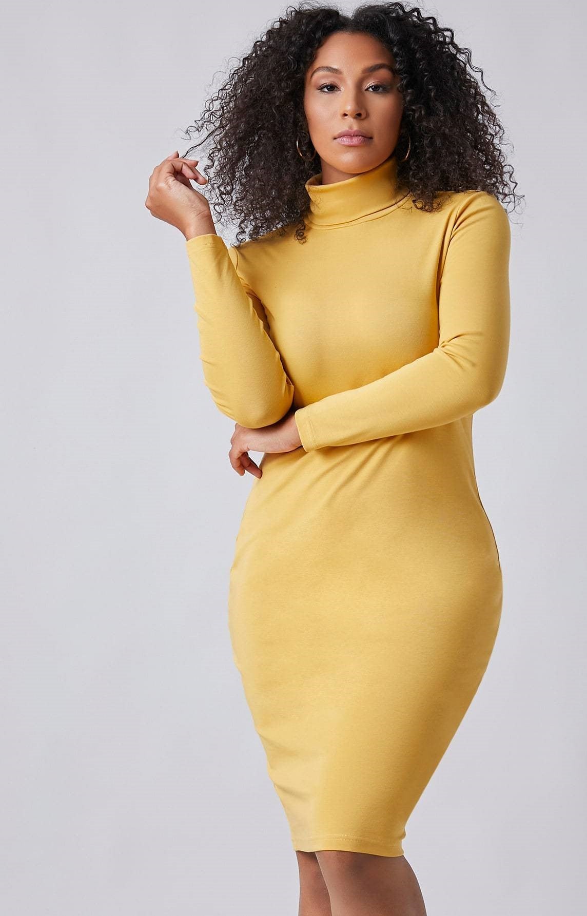 A person models wearing the Bright & Delight Spring Dress, a fitted yellow turtleneck dress from BCNY BOUTIQUE, posing with one hand on their hip and the other near their face against a plain background.