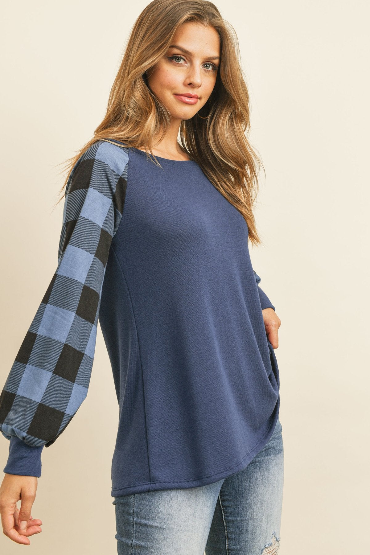 A woman wearing a faded denim plaid puff sleeved round neck top by Riah Fashion and ripped jeans stands against a plain background.