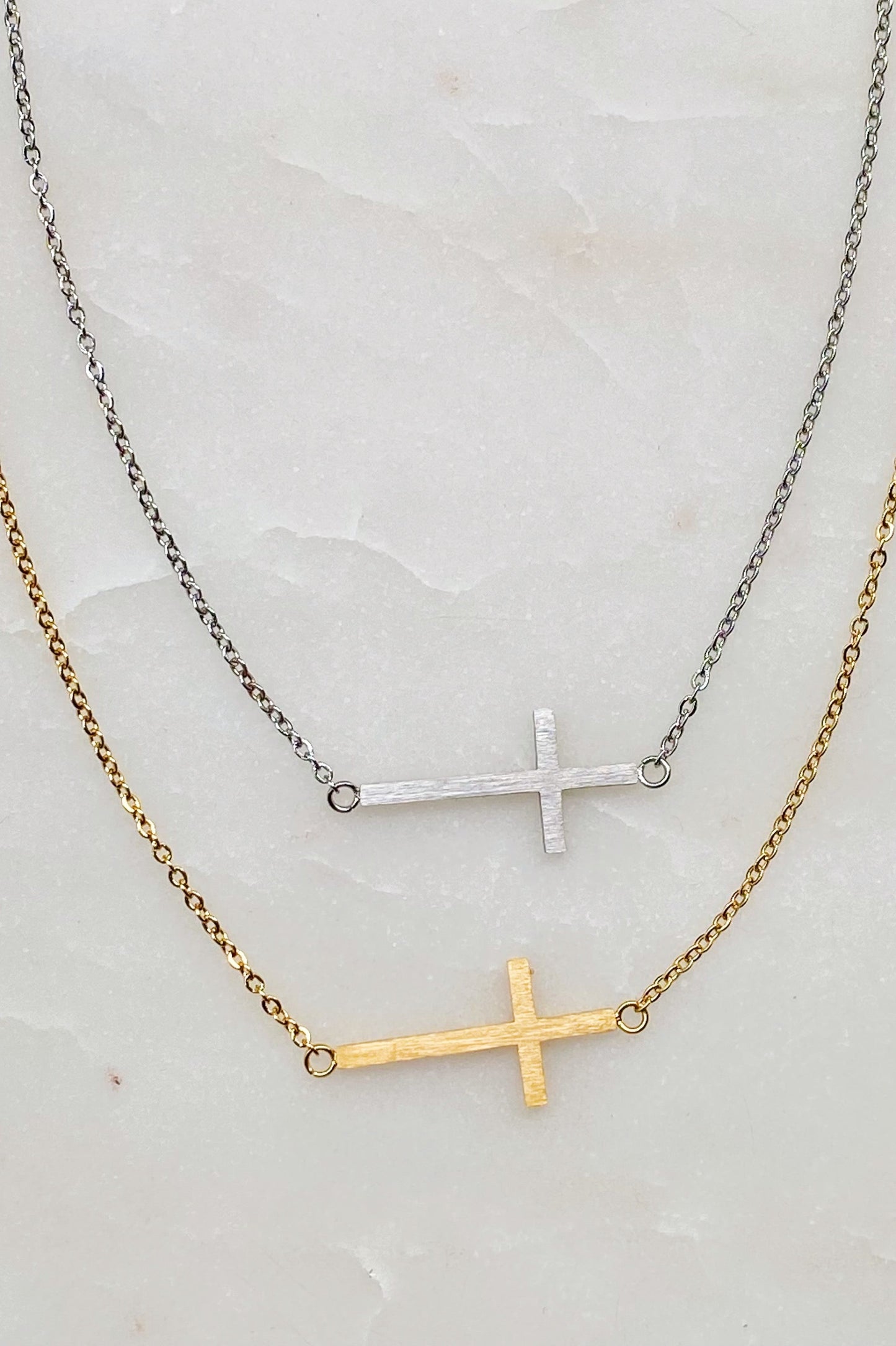Two Kayla Cross Necklaces from Ellison + Young, one silver and one gold, presented on a white surface.