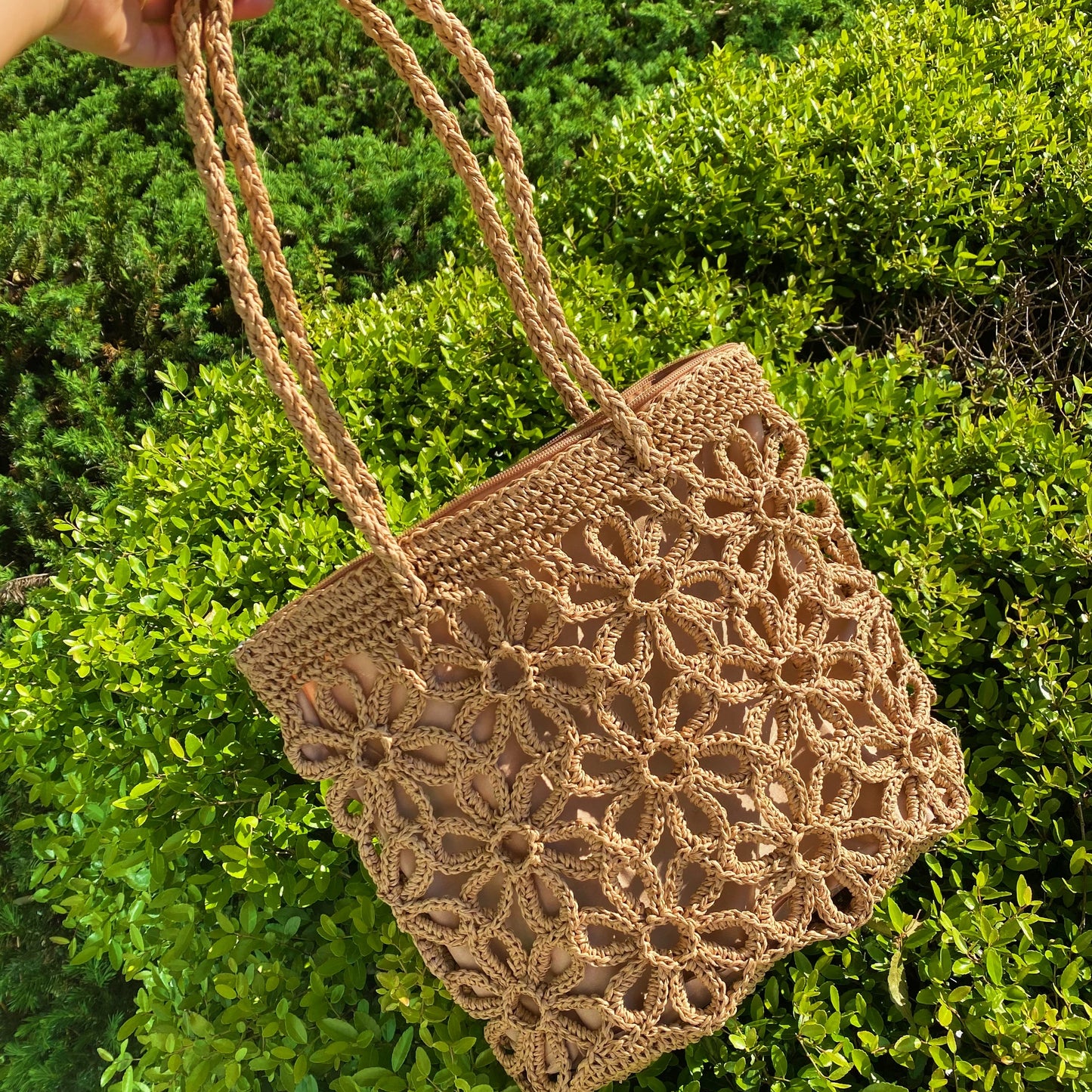 A person smiles while standing outdoors with a clear blue sky and trees in the background, wearing a yellow striped sweater and holding an Ellison + Young Hand Made Muted Floral Tote.