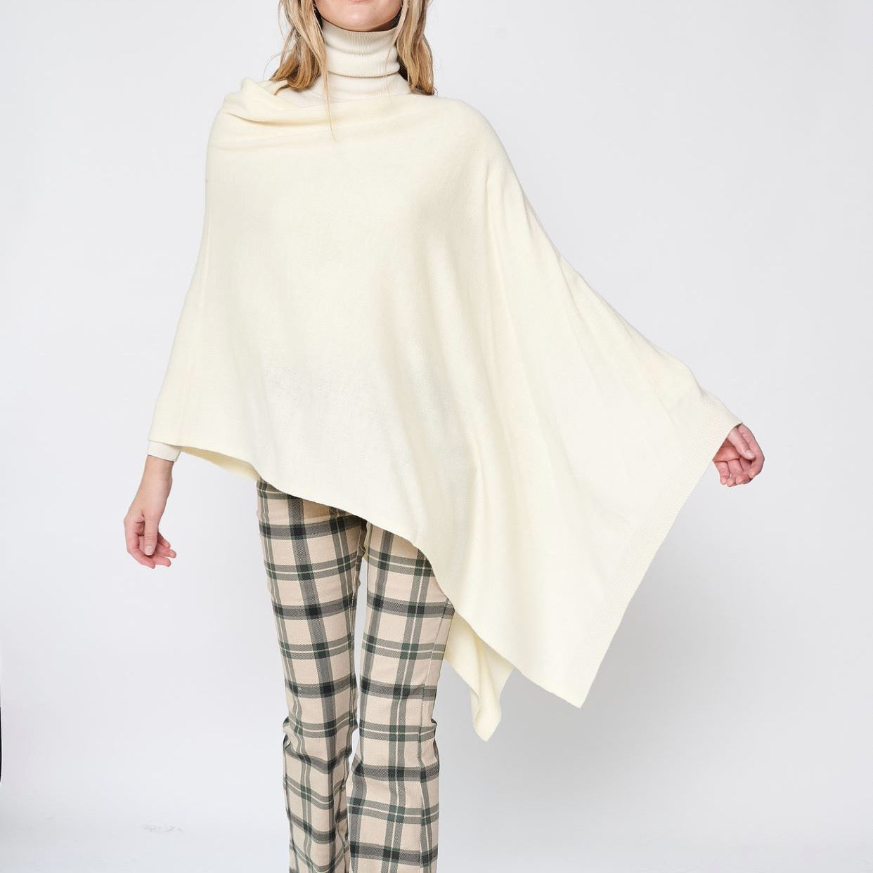 Someone wearing the Take With Me Travel Poncho by Ellison + Young with plaid pants against a plain white background.